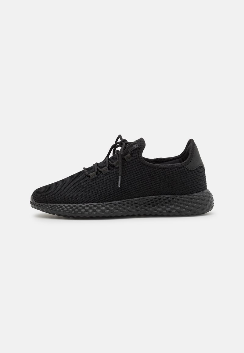 Baskets athlétiques noires avec semelle texturée, tige en mesh et fermeture à lacets, présentées de profil sur un fond neutre.