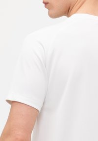Weiße Kurzarm-T-Shirt mit glatter Textur, Rundhalsausschnitt und aufgeschlagenen Ärmeln. Sichtbare Schulternahtdetails heben das Design hervor.