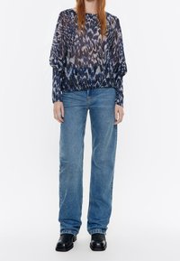 Langsleeve, gemuste blouse in diepblauw en grijs, gecombineerd met losvallende lichtblauwe denim jeans en zwarte enkelboots.
