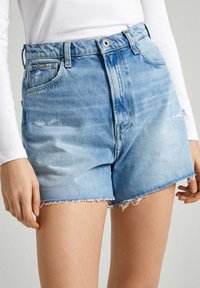 Shorts de mezclilla de tiro alto en azul claro con detalles desgastados, dobladillo deshilachado y diseño de cinco bolsillos. Cuenta con trabillas para cinturón y cierre frontal con botón.