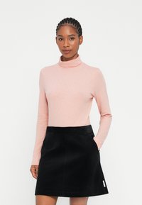 Lys rosa langermet turtleneck kombinert med et svart cordfløyel A-line skjørt med sidelommer og en liten merkelapp på kanten.