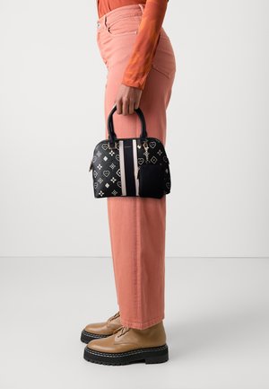 Person in coral pants and orange top holding a small black handbag with patterned design and beige boots on a white background.