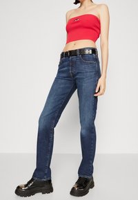 Högmidjade blå denimjeans med raka ben, knapp- och dragkedjestängning, kombinerat med en röd ribbad crop top och svarta chunky platåskor.