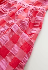 Tissu à carreaux rouge et rose avec une texture froncée, présentant une taille froncée et un éclat doux, mettant en valeur les carrés contrastés.