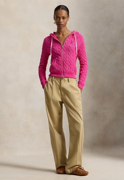 Ροζ φούτερ με φερμουάρ και πλεκτό σχέδιο καλώδιο, με λευκά κορδόνια, συνδυασμένο με καφέ παντελόνια ψηλής μέσης και καφέ μοκασίνια.