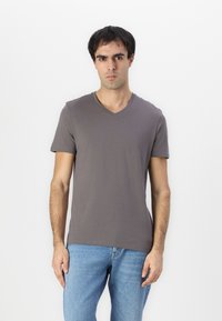 Graues, kurzärmliges V-Neck-T-Shirt aus weicher Baumwolle mit schmalem Schnitt und dezentem Logo-Detail auf der Brust, kombiniert mit hellblauen Jeans.