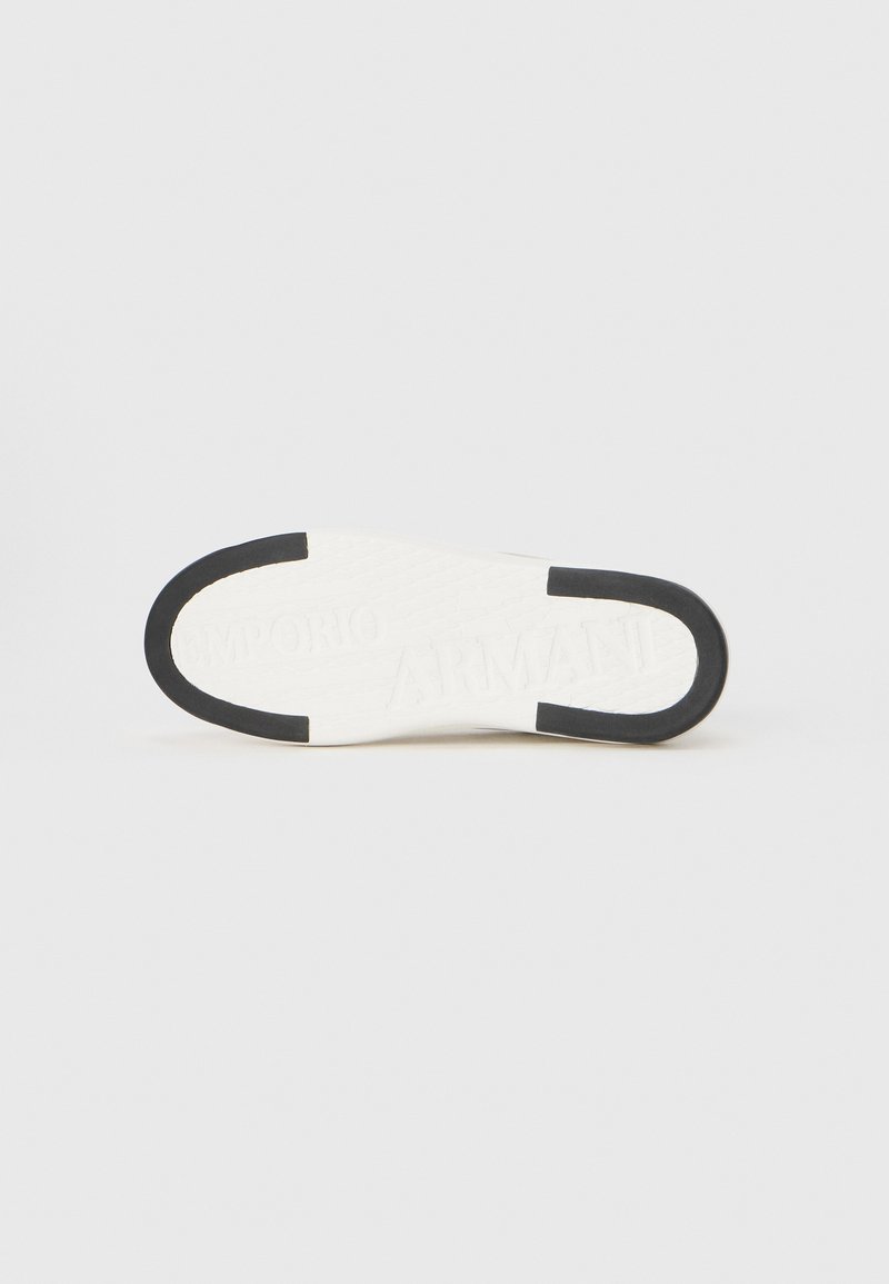 Sole di sneaker bianca con accenti neri e motivo di grip testurizzato. Presenta la scritta in rilievo "Emporio Armani". Design pulito e minimalista.