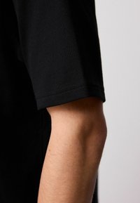 Sort kortærmet bomulds T-shirt med en glat tekstur, der har en ren skæring ved ærmet og en diskret sømdetalje.