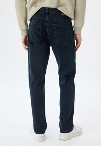 Pantalones vaqueros de mezclilla azul oscuro con un corte recto, cinco bolsillos y una etiqueta de cuero en la cintura. Terminados con una textura suave.