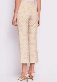 Pantaloni beige a lunghezza caviglia con una vita aderente e un motivo a diamante. Abbinati a mule color crema con tacco accentato in oro.