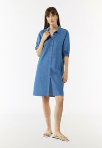 Sukienka koszulowa z denimu, jasnoniebieska, z krótkimi rękawami i elastycznymi mankietami, zapinana na guziki, z kieszonką naszywaną, do kolan, noszona z sandałami na paski.