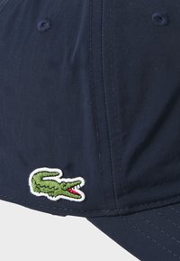 Ναυτικό καπέλο μπέιζμπολ από λείο ύφασμα με κεντημένο λογότυπο πράσινου κροκόδειλου. Διαθέτει ραμμένα λεπτομέρειες και κανονικό χείλος.