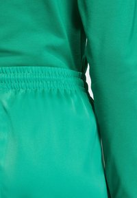 Green clothing featuring a textured, stretchy fabric; smooth, fitted top with long sleeves; elastic waistband on loose-fitting pants.