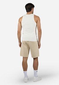 Top blanco sin mangas, pantalones cortos beige, zapatillas blancas y calcetines blancos. La ropa presenta un diseño ajustado con textura acanalada y un estilo casual.