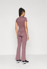 Κοντομάνικη μπλούζα εφαρμοστού τύπου και φαρδιά παντελόνια σε λιγότερο έντονο μωβ ύφασμα, με λεία υφή, συνδυασμένα με μαύρα αθλητικά παπούτσια.