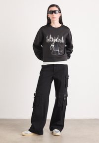 Sweatshirt preto com um gráfico de paisagem urbana, combinado com calças cargo largas pretas com múltiplos bolsos e detalhes em prata.