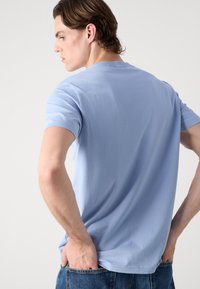 Světle modré tričko s krátkým rukávem vyrobené z bavlny. Má kulatý výstřih a volný střih, s hladkou strukturou a minimalistickým designem.