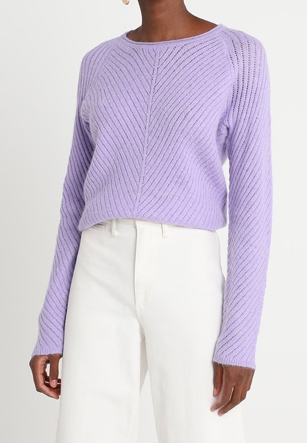 Pull en tricot texturé lilas avec un col rond et des manches longues côtelées. Présente un motif chevrons et une coupe décontractée. Associé à un pantalon blanc.