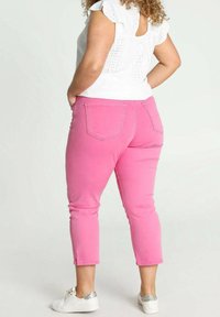 Růžové zkrácené kalhoty s úzkým střihem, s kapsami na zadní straně a bočním rozparkem. Nosí se s bílou blůzou a bílými botami se stříbrnými akcenty.