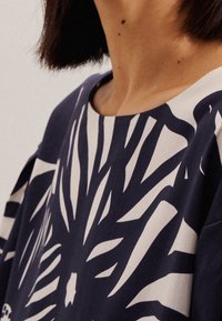 Top blu navy con una stampa botanica bianca audace, scollatura rotonda e maniche corte, realizzato in tessuto leggero e morbido.