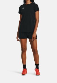 Black athletic t-shirt and shorts made from breathable fabric. Red soccer cleats with textured design. Plain background.