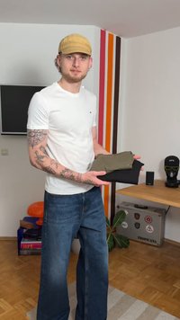 Gray and black t-shirts held by a person in a white t-shirt and blue jeans. The room features colorful stripes and modern decor.