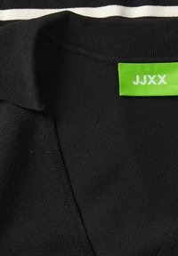 Juodas megztinis su V formos iškirpte, pagamintas iš minkštos medžiagos. Puoštas žalia etikete su "JJXX" ir balta juostele šalia apykaklės.