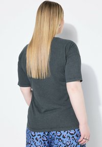 Camiseta de algodón gris oscuro con un corte relajado, mangas cortas y cuello redondo. Costuras visibles y detalles de diseño mínimos.