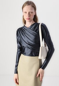 Marine sateng topp med drapert design, lange ermer, kombinert med et beige skinnskjørt og en liten kremfarget håndveske. Glatte, stilige teksturer.