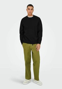 Black sweater, olive green pants, and white sneakers. The sweater has a round neck and ribbed cuffs, while pants are straight-leg with side pockets.