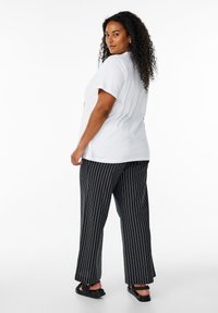 T-shirt bianco in cotone abbinato a pantaloni larghi a righe verticali nere e sandali neri. I pantaloni presentano una vestibilità comoda e sottili righe verticali.
