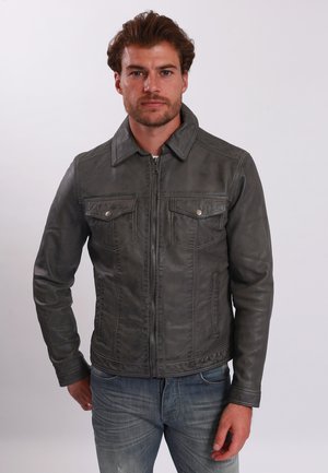 Chaqueta de cuero gris con cierre delantero, dos bolsillos en el pecho y un cuello puntiagudo. Presenta detalles cosidos y una textura suave. Lleva puesta con jeans.