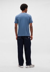 Gaiši zilā īsroku krekls ar apaļu kakla izgriezumu, kopā ar tumši zilām vaļīgām džinsām. Balti sporta apavi ar akcentiem papildina apģērbu.