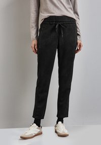 Zwarte suède joggerpants met een slim fit, elastische taille met trekkoord en zijzakken met ritssluiting, gecombineerd met witte en tan sneakers.