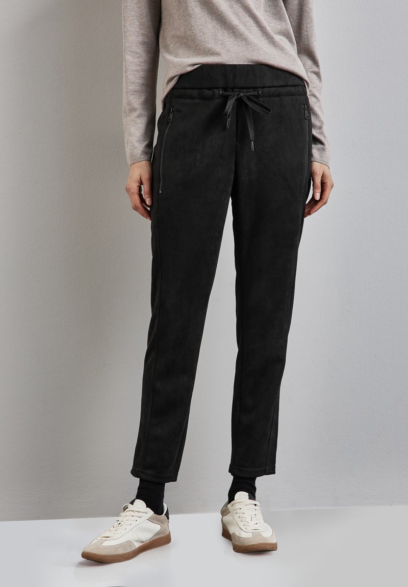 Zwarte suède joggerpants met een slim fit, elastische taille met trekkoord en zijzakken met ritssluiting, gecombineerd met witte en tan sneakers.