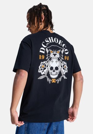 Zwart katoenen T-shirt met een grafisch ontwerp met een panter, schedel en bloemmotieven, met de tekst "DCSHOECO" en "1994" in oranje en wit.