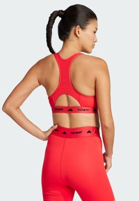 Sujetador deportivo rojo y leggings a juego, fabricados con material liso y elástico. Las características incluyen un diseño de espalda nadadora y cinturas de marca en negro.