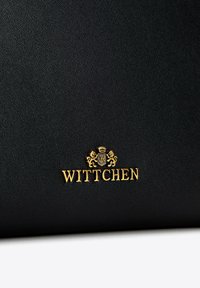 Borsa in pelle nera con texture, caratterizzata da un logo dorato "Wittchen" con una corona e dettagli di design a forma di leone nella parte inferiore.