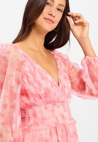 Pink floral dress with sheer balloon sleeves, a deep V-neck, and a gathered waistline. The fabric features a soft, textured finish.