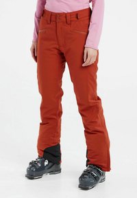 Pantaloni da sci arancioni con design a gamba dritta, due tasche frontali e una texture liscia. Indossati con stivali da sci neri.