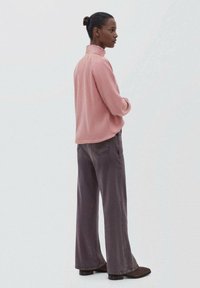Blusa rosa a maniche lunghe con colletto alto, abbinata a pantaloni grigi a gamba larga e stivali alla caviglia marroni scuri. Texture del tessuto liscia.
