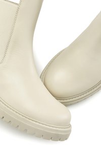Bež čizme do gležnja izrađene od glatke kože, s elastičnim bočnim panelima, zaobljenim vrhom i teksturiranim gumenim potplatima s izraženim uzorkom.