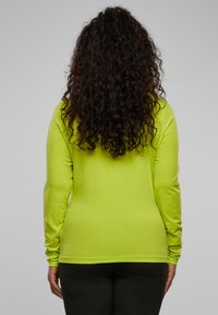 Langermet limegrønn skjorte laget av glatt stoff, med en tettsittende design og rund hals, brukt med svarte bukser.