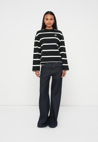 Haut à manches longues à rayures noir et blanc en coton, avec col rond et détail brodé. Associé à un jean large taille haute bleu foncé.