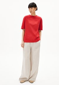 Rode katoenen t-shirt met korte mouwen en een ronde hals, gecombineerd met losse beige linnen broeken. Eenvoudig ontwerp zonder opvallende patronen.
