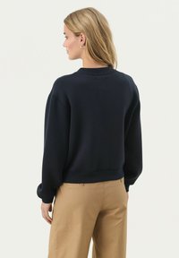 Tengerészeti oversized pulóver bordázott mandzsettákkal és aljjal, puha textúrával, kerek nyakkivágással, khaki nadrággal bemutatva.