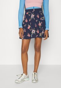 Gonna blu navy con stampa floreale e vita elastica, decorata con fiori rosa e verdi, abbinata a una maglietta a maniche lunghe blu e sneakers argento.