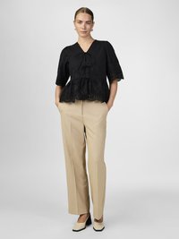Črni peplum top z očesnimi detajli in sprednjim vezanjem, v kombinaciji z bež visokimi hlačami in kremnimi čevlji z črnimi poudarki.