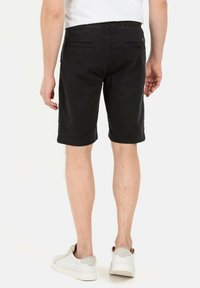 Schwarze Denim-Shorts mit regulärer Passform, Gesäßtaschen und glatter Textur, kombiniert mit weißen Sneakers, was einen lässigen Look zeigt.