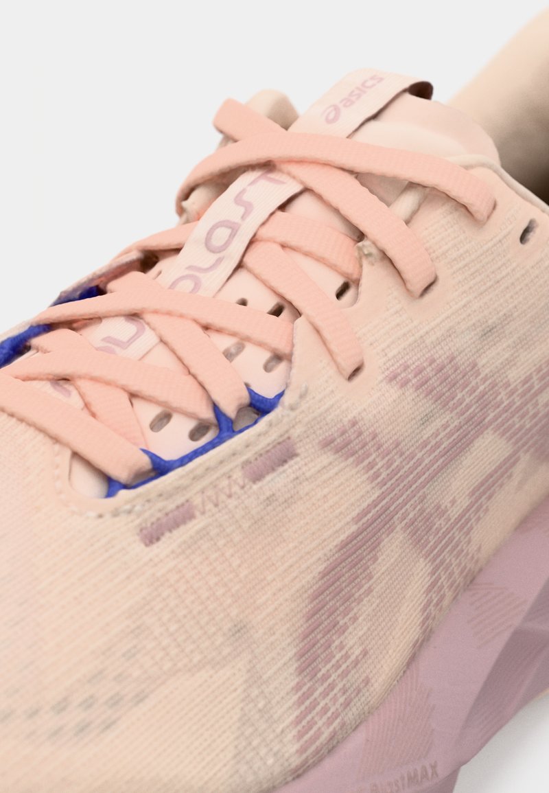 Baskets de course rose clair avec une tige texturée, portant des lacets roses et un accent bleu sur la languette. Amorti doux et design élégant.